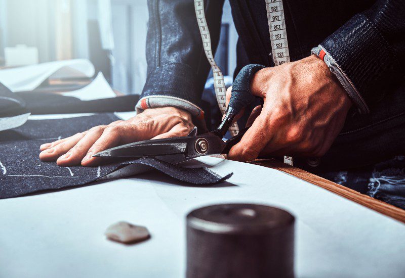 Custom Overcoats in Chicago A person from Richard Bennett Custom Tailors is cutting a piece of cloth in Chicago, IL
